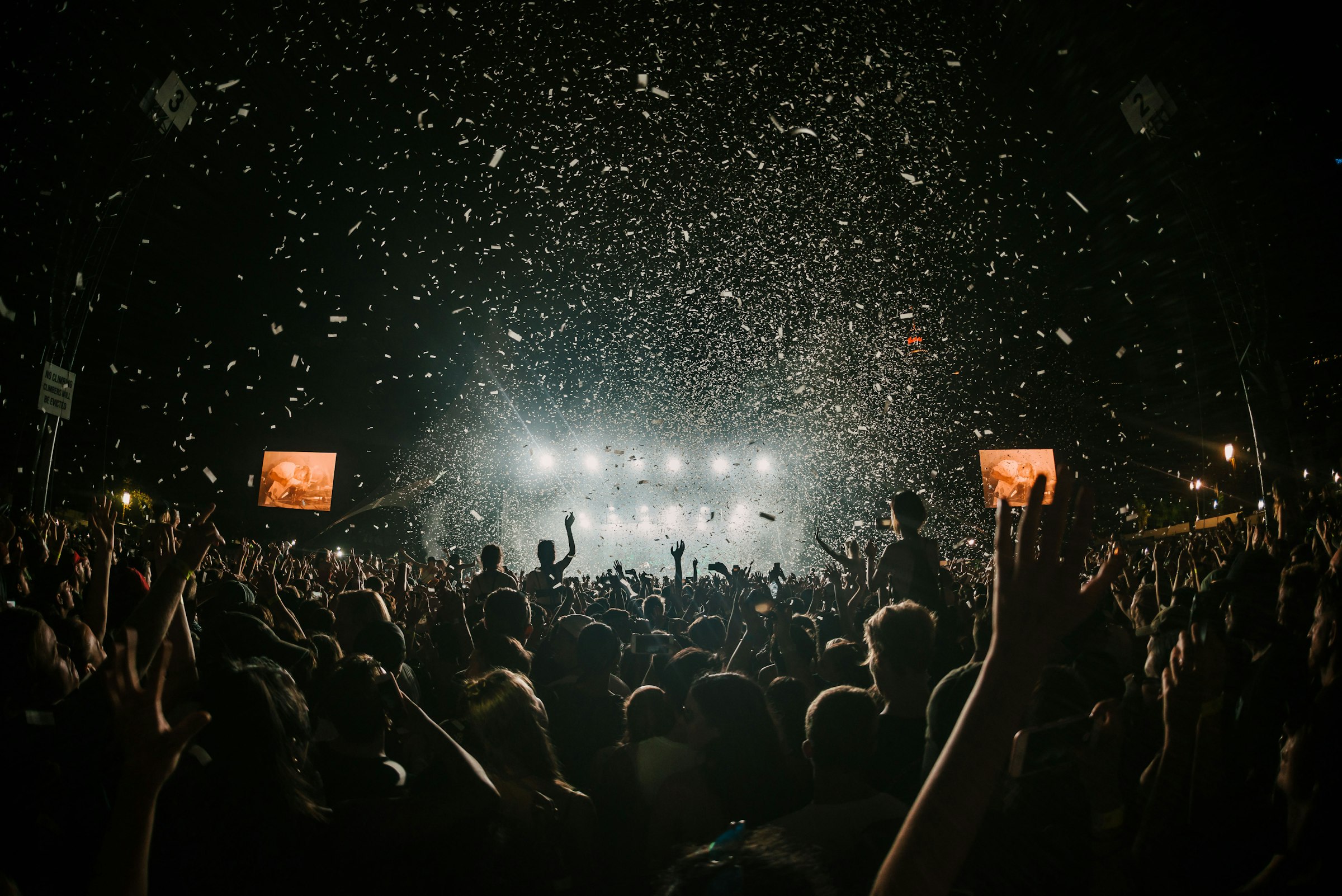 Festival crowd under stage lights and confetti at night